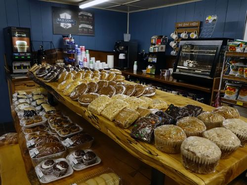 A display of various baked goods, including cookies, muffins, and pastries, on a wooden table in a cozy café.