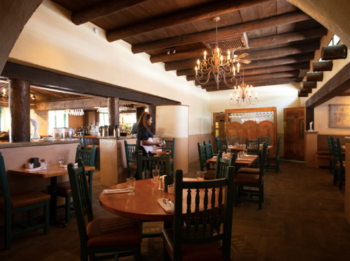 Cozy restaurant interior with wooden beams, tables set for dining, and a warm ambiance.