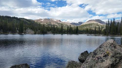 A serene lake surrounded by mountains and lush green trees under a partly cloudy sky.