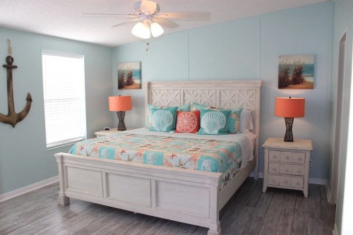 Brightly decorated bedroom with a large bed, colorful pillows, orange lamps, and beach-themed artwork on light blue walls.