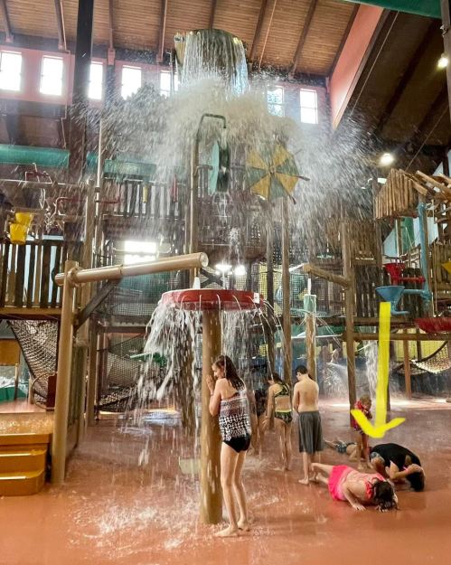 Children playing in a water park with a large water feature pouring down, creating a fun, splash-filled environment.