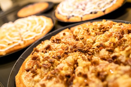 A close-up of a dessert pizza topped with nuts and caramel, with other pizzas in the background.
