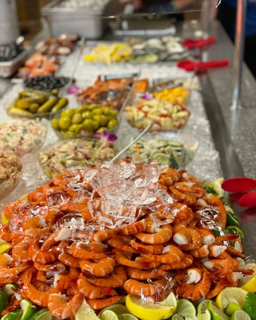 A vibrant seafood display featuring a large mound of shrimp on ice, surrounded by various garnishes and side dishes.