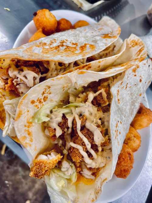 Two crispy chicken tacos with lettuce and sauce, served with golden-brown fried snacks on the side.