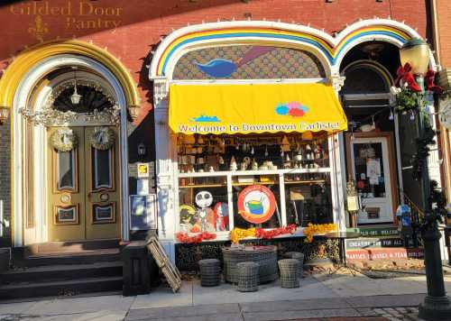 Colorful storefront with a yellow awning reading "Welcome to Downtown Carlisle," decorated for the season.