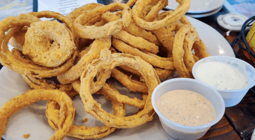A plate of crispy, golden-brown onion rings served with two dipping sauces.