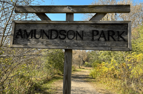 Wooden sign for Amundson Park along a nature trail, surrounded by greenery and trees.