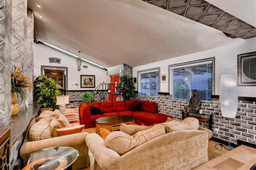 Cozy living room with red and beige sofas, decorative plants, and a statue, featuring a modern design and warm lighting.
