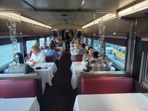 Interior of a dining train car with tables set for meals, featuring diners enjoying their food and drinks.