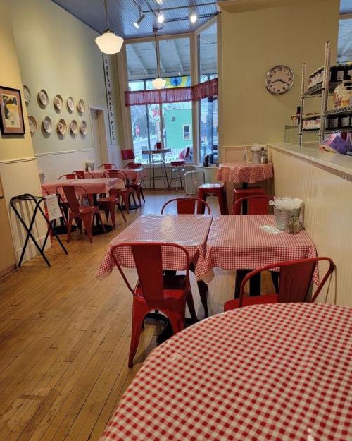 Cozy café interior with red-checkered tablecloths, wooden floors, and bright natural light.