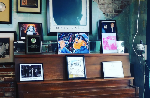 A wooden piano adorned with framed photos and artwork, set against a brick wall in a cozy space.