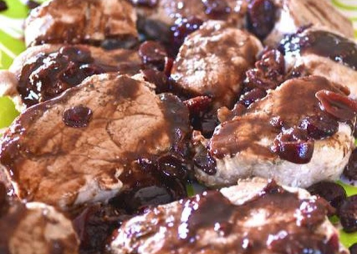 Sliced pork chops topped with a rich, dark cherry sauce on a green plate.