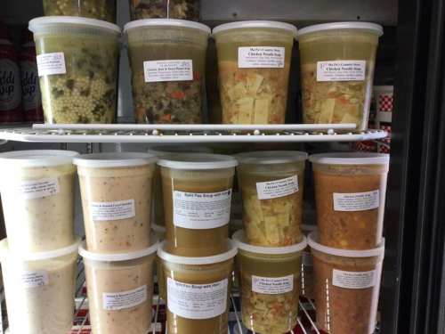 Containers of various soups and stews on shelves, each labeled with ingredients and names.