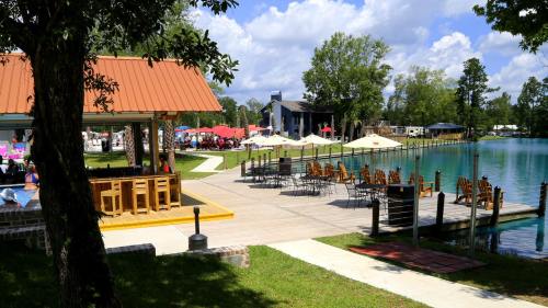 A scenic lakeside area with a pavilion, seating, and umbrellas, surrounded by trees and a clear blue sky.