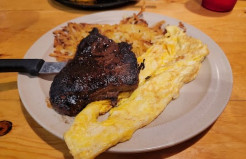 A plate with a charred steak, fluffy scrambled eggs, and crispy hash browns on a wooden table.