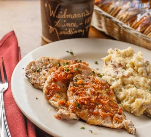 Plate of seasoned pork chops topped with chopped onions, served with creamy mashed potatoes and a rustic jar in the background.