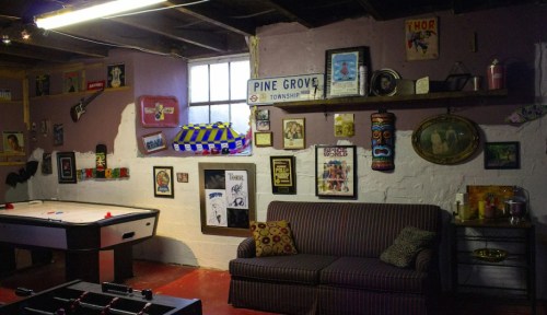 A cozy basement with a sofa, game tables, and walls adorned with various vintage posters and decorations.