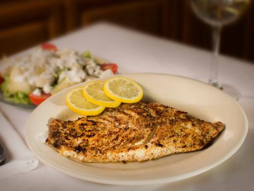 A plate of grilled fish garnished with lemon slices, served alongside a fresh salad.