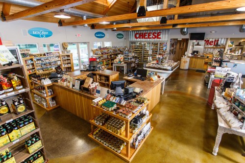 A spacious store interior with wooden shelves filled with various products, a cheese section, and a checkout area.