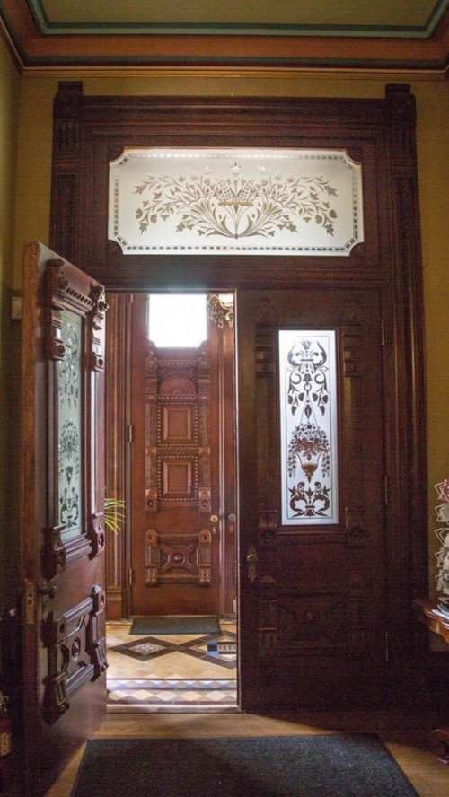 Intricately designed wooden doors open to a grand entryway with decorative glass panels and ornate details.
