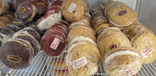 A variety of wrapped cookies, including peanut butter and oatmeal raisin, displayed on a shelf.