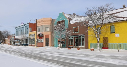 A snowy street scene featuring colorful buildings and trees, with a clear blue sky above.