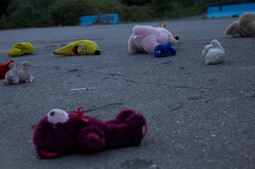 A scattered collection of stuffed animals and toys lying on a gray pavement in an outdoor setting.