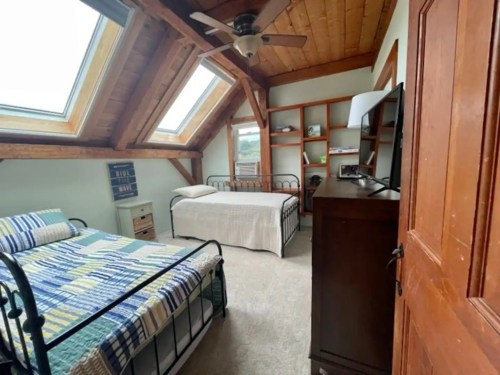Cozy attic bedroom with two beds, skylights, wooden beams, and a TV on a dresser.