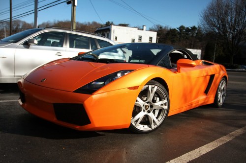 An orange Lamborghini Gallardo convertible parked on a street, showcasing its sleek design and shiny alloy wheels.
