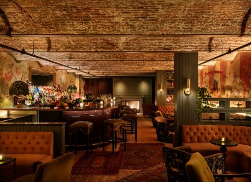 Cozy bar interior with brick walls, plush seating, and a well-stocked bar illuminated by soft lighting.