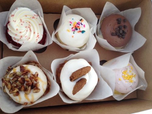 A box of six assorted cupcakes with various toppings, including sprinkles, chocolate chips, and nuts.