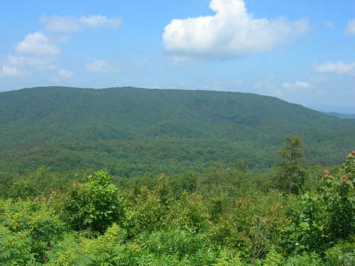 Lush green mountains under a blue sky with fluffy clouds, showcasing a serene natural landscape.