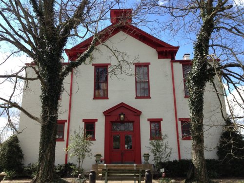 A white building with red trim and windows, flanked by bare trees, under a blue sky.