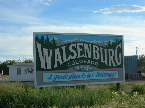 Welcome sign for Walsenburg, Colorado, featuring mountains and greenery, with a bright blue sky in the background.