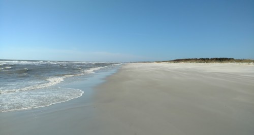 A serene beach scene with gentle waves, soft sand, and a clear blue sky stretching into the horizon.