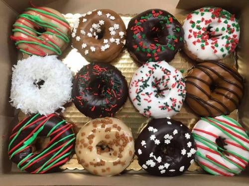 A box of 12 festive donuts, decorated with colorful icing, sprinkles, and toppings for the holiday season.