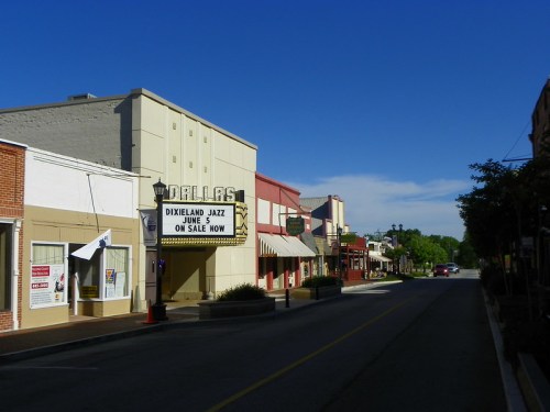 A quiet street in Dallas with shops and a marquee advertising a Dixieland Jazz event. Clear blue sky above.