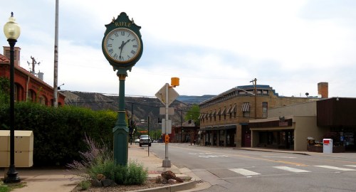A street view of Rifle, Colorado, featuring a vintage clock and historic buildings against a mountainous backdrop.