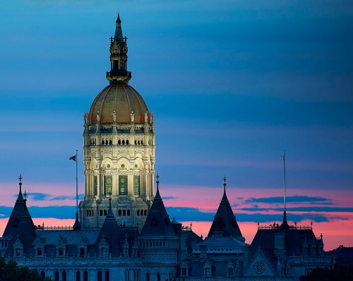 The Connecticut State Capitol building at dusk, illuminated against a colorful sky.