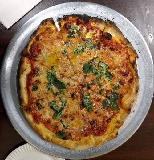 A round pizza topped with cheese, tomato sauce, and fresh green herbs, sliced into eight pieces on a metal tray.