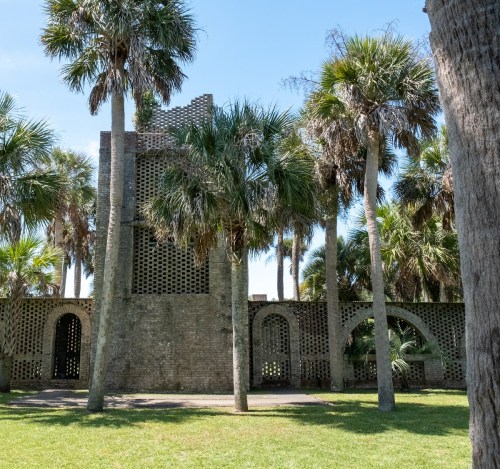 A stone structure surrounded by tall palm trees under a clear blue sky.