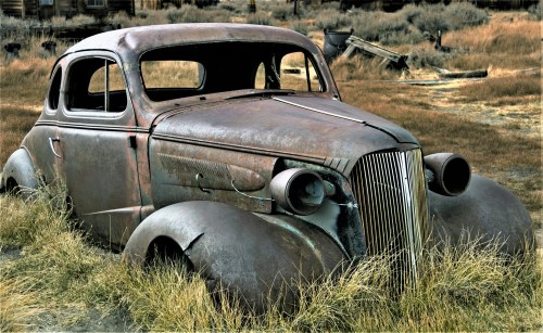 An old, rusted car sits abandoned in tall grass, showcasing its vintage design and weathered features.