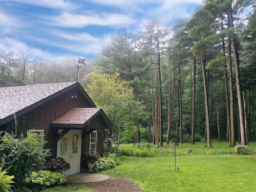 A cozy cabin surrounded by lush greenery and tall trees under a blue sky with scattered clouds.