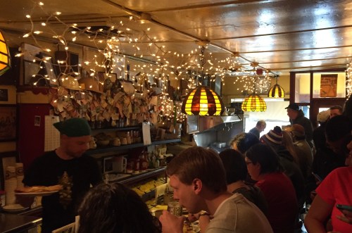 A cozy café filled with patrons, warm lighting, and festive decorations, creating a lively and inviting atmosphere.