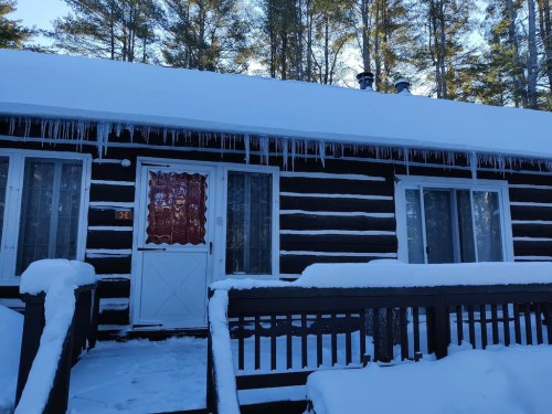 A cozy log cabin covered in snow, with icicles hanging from the roof and a welcoming front door.