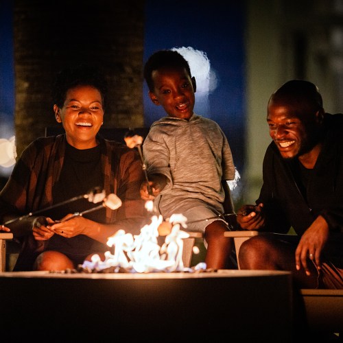 A family gathers around a fire pit at night, enjoying each other's company and warmth.