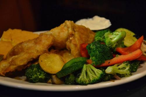 A plate of fried fish with broccoli, mixed vegetables, and a side of dipping sauce.