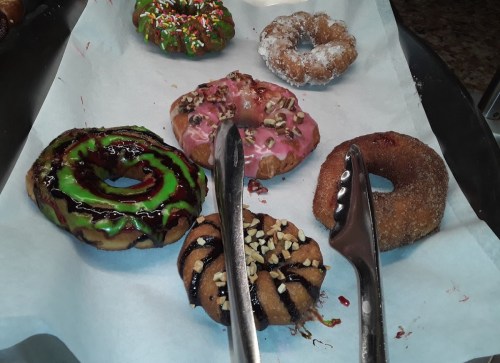 A variety of colorful donuts on parchment paper, including glazed, sprinkled, and chocolate-drizzled options.