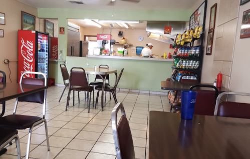 A casual dining area with tables, a Coca-Cola vending machine, and a kitchen in the background.