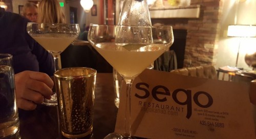 Two martini glasses on a table with a menu for Sego Restaurant in a cozy, dimly lit setting.